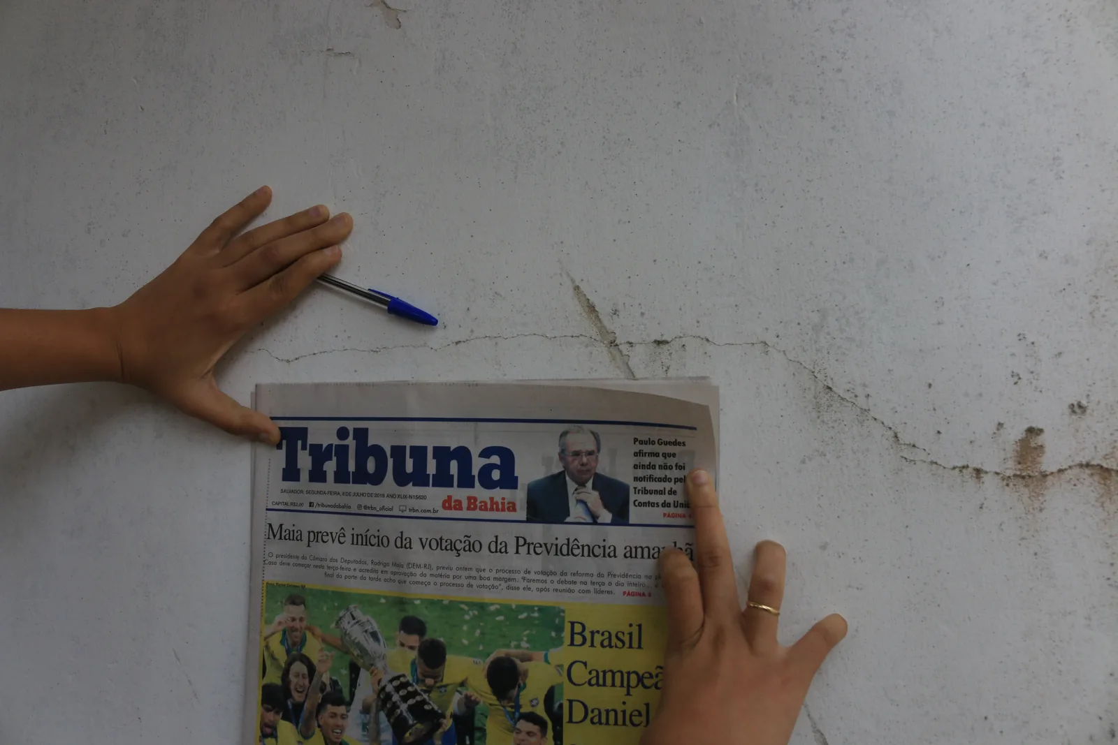 Fissura em parede interna com o jornal Tribuna da Bahia, de 8 de julho de 2019, apoiado ao lado como referência de data.